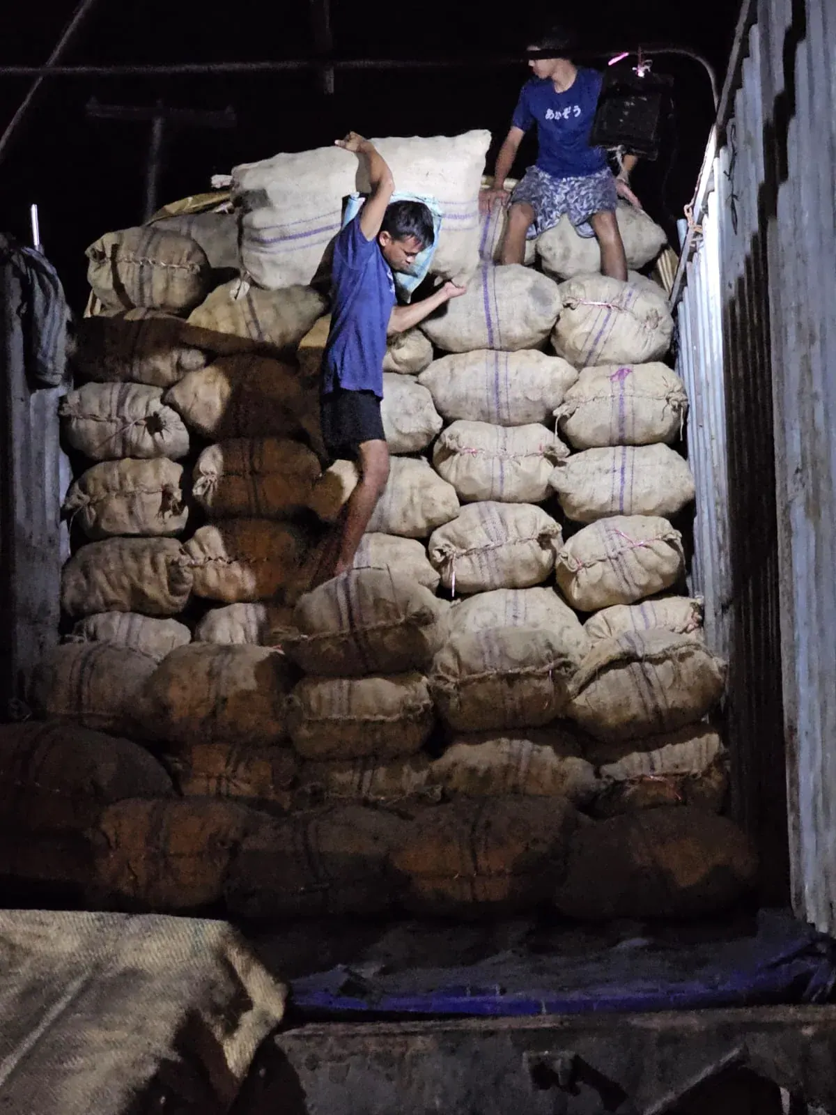 Workers handling bags at the rear of an open truck bed